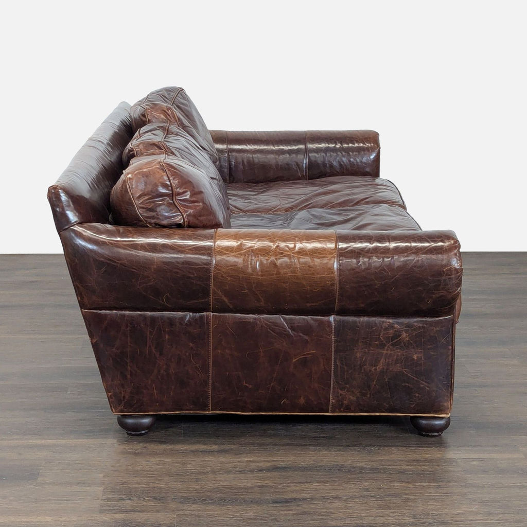 Side view of a brown leather Restoration Hardware 3-seat sofa, showing deep seating and worn, classic upholstery.