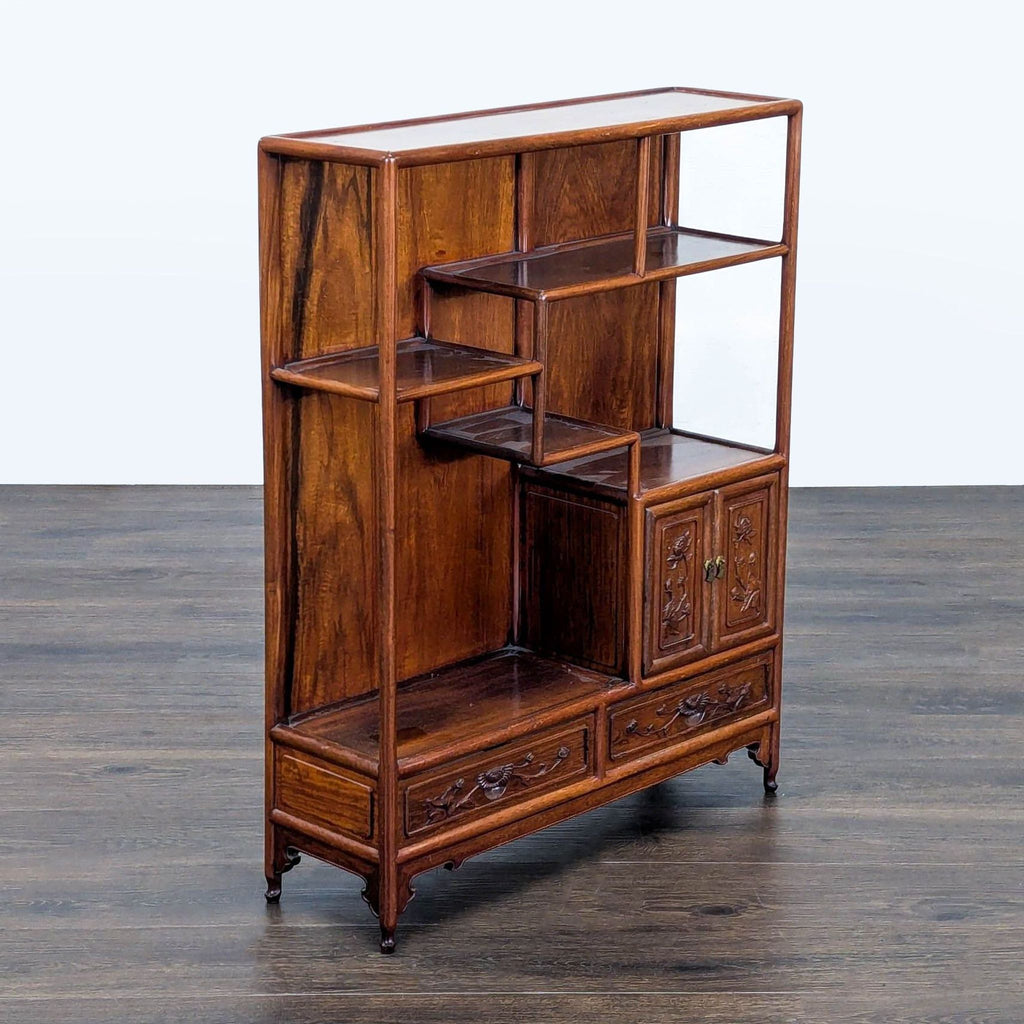Bookshelf with a tiered design, featuring open shelves, a small cabinet with decorative doors, and carved drawers.