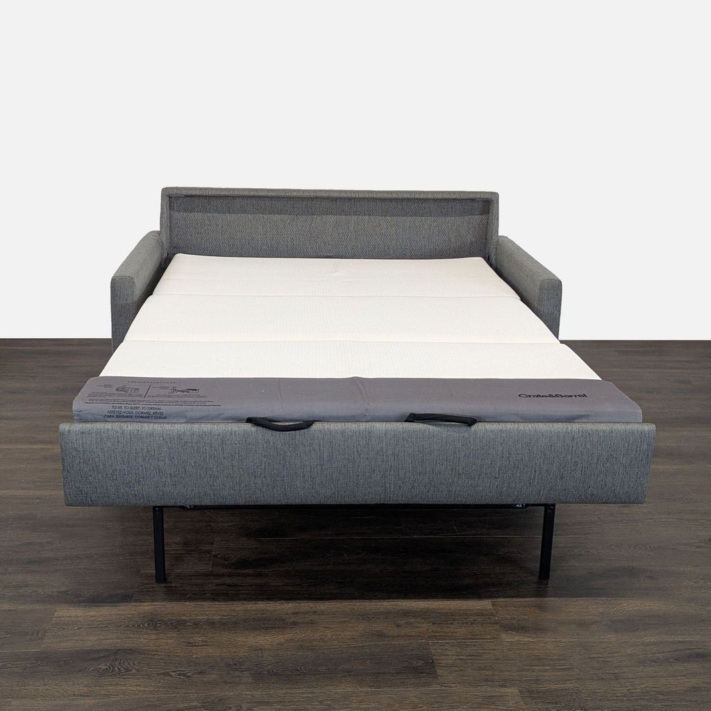 Stylish gray sleeper sofa by Crate and Barrel, featuring tufted cushions and functional pull-out bed.