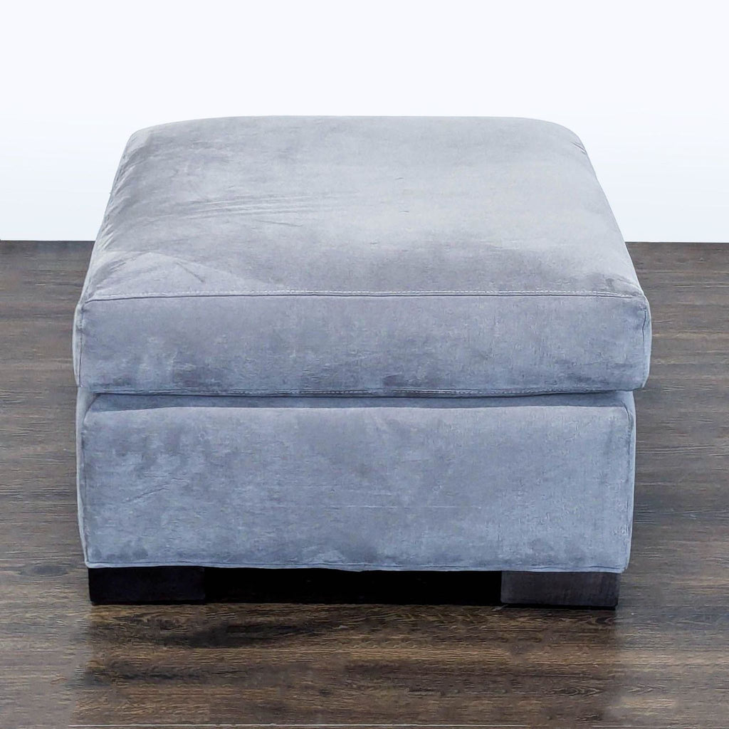 2. Square gray velvet ottoman from Crate & Barrel, viewed from the front, featuring a soft, padded top.