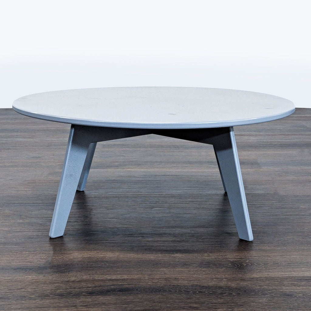 Sleek, round Room and Board table with a light grey finish and modern outdoor design, showing minor wear.