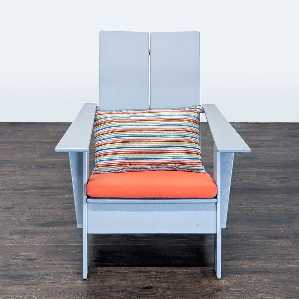 A modern Adirondack chair by Room & Board with a light gray frame, orange cushion, and striped pillow.