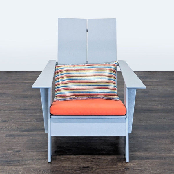A modern Adirondack chair by Room & Board with a light gray frame, orange cushion, and striped pillow.