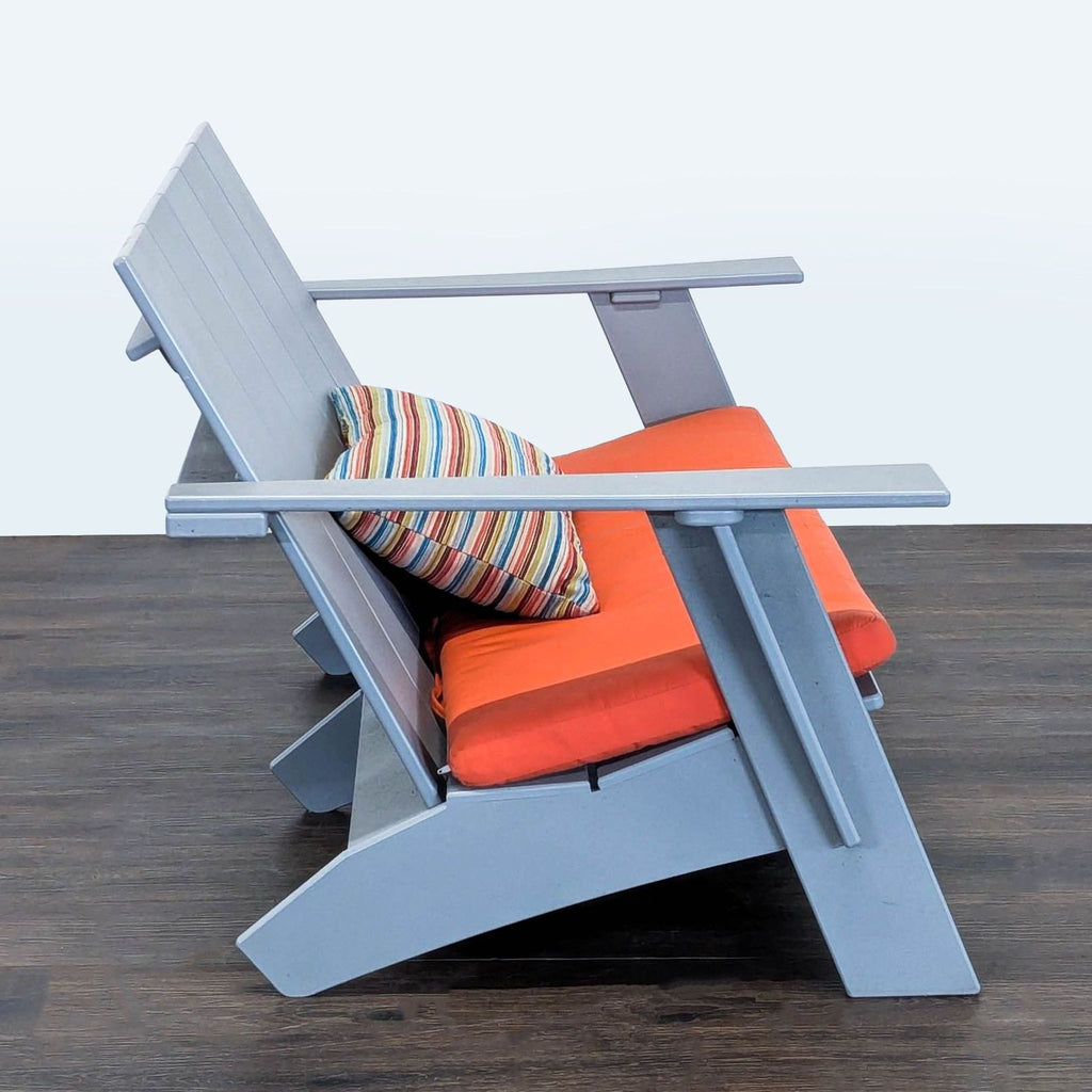 Contemporary gray-framed loveseat by Room & Board, features bright orange seat and vibrant striped pillow.