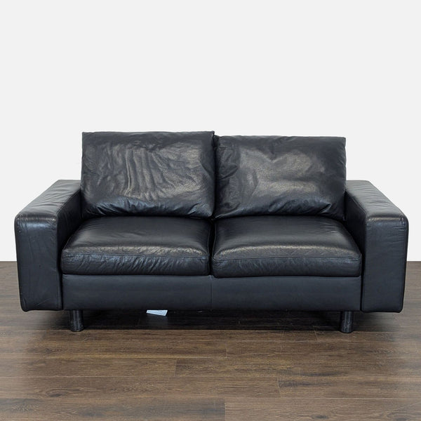 Black leather Ekornes Stressless loveseat with modern design, plush cushions, and boxy silhouette for comfort.