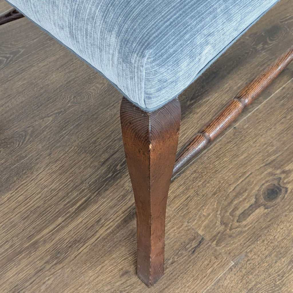 3. Close-up of a dining chair’s cabriole front leg and blue upholstered seat over wood flooring.