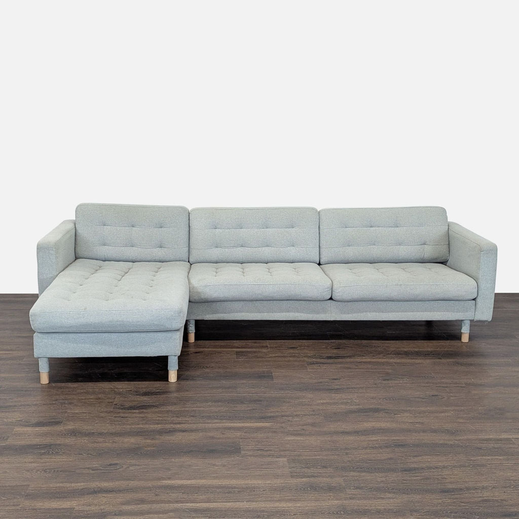 Light gray Ikea sectional with chaise, tufted cushions, and wooden legs in a modern living room setting.