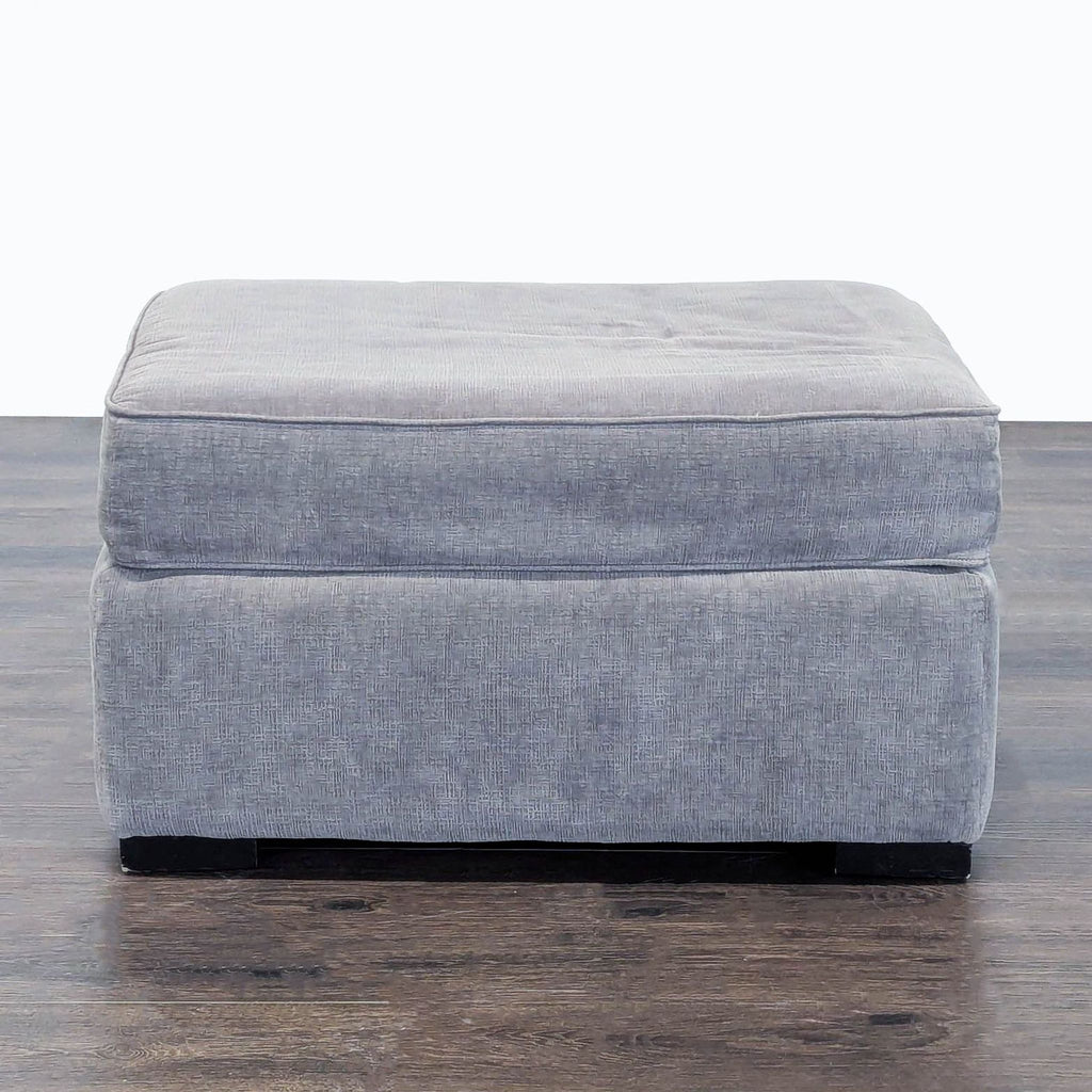 2. Front view of a rectangular gray fabric ottoman, featuring a plush top and simple modern design.
