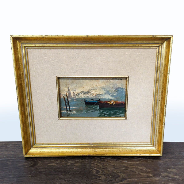 Small painting of two boats on water beneath soft clouds, set in an elegant gold frame with fabric mat.
