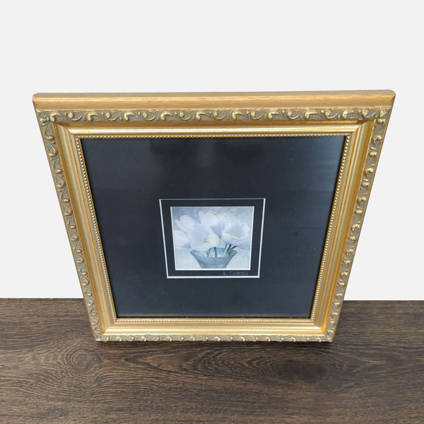 Floral print by L. Eastwood shows white flowers in a vase, set in black mat and gold frame.