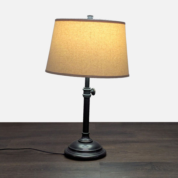 Adjustable table lamp with a dark metal base and beige fabric shade, ideal for desks or bedsides.