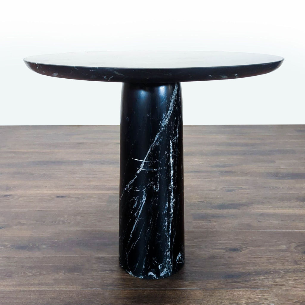 Sculptural black marble dining table featuring a smooth, round top and a tapered base, designed by Mermelada Estudio.
