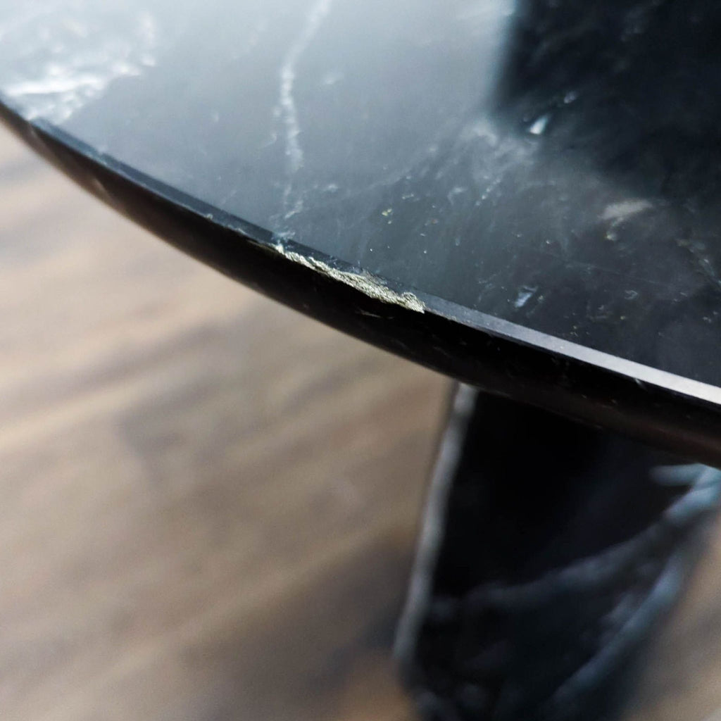Modern black marble dining table by CB2 with elegant rounded top and a sleek, tapered pedestal base.