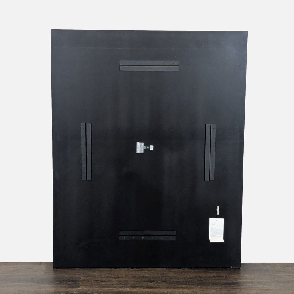 3. Backside of the CB2 black geometric wall panel, showing mounting hardware and a product tag against a plain background.
