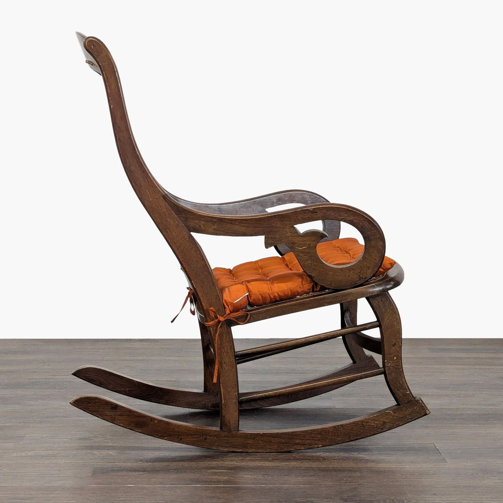 Wooden rocking chair with woven cane backrest and orange cushion, featuring curved armrests and timeless style.