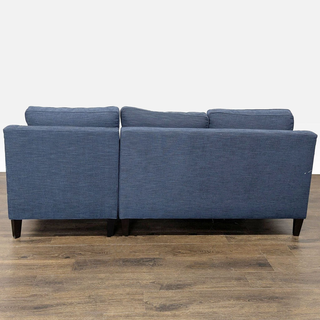 3. Rear view of a blue Pottery Barn sectional sofa with sturdy dark wood legs and comfortable back cushions.