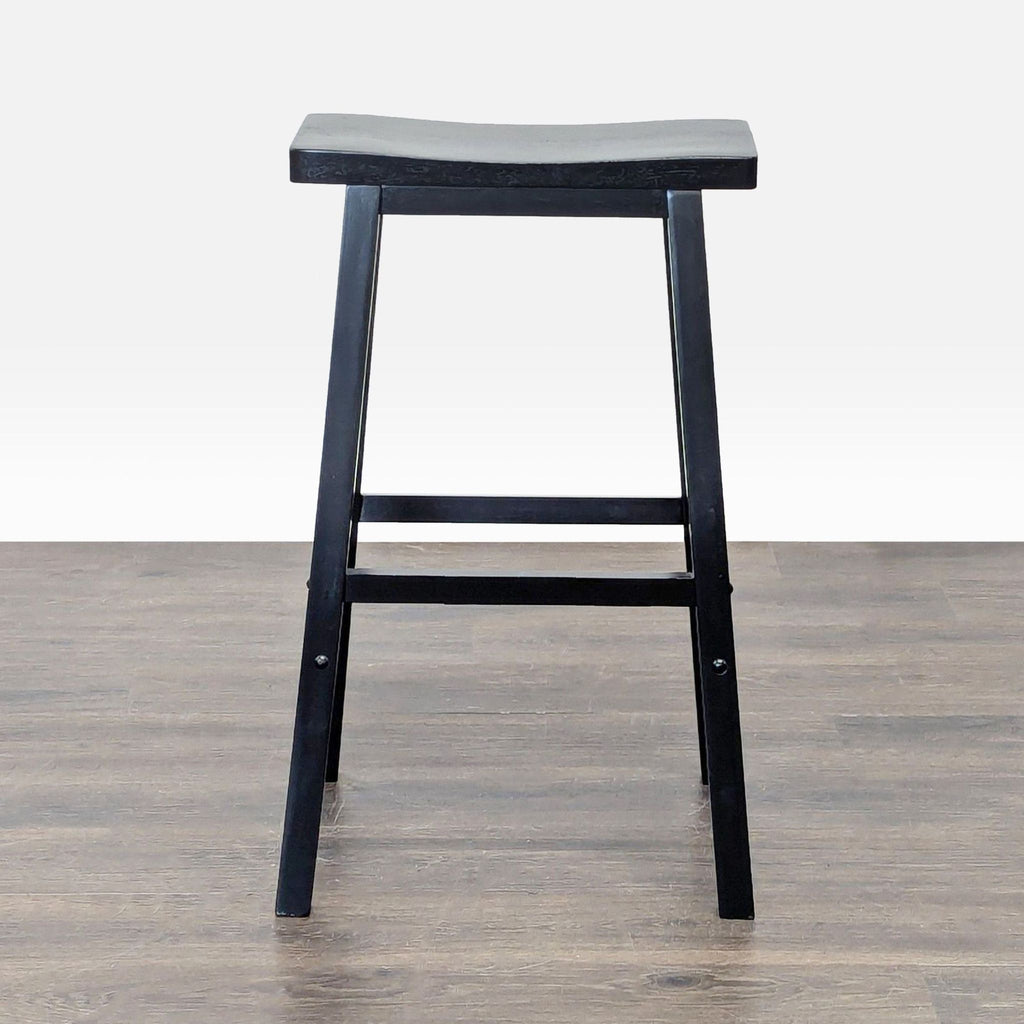 1. Black wooden bar stool with a saddle-shaped seat, viewed from the front on a wood floor.