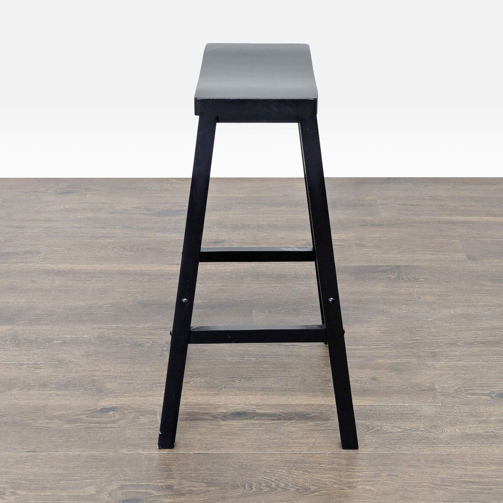 2. Side profile of a black wooden bar stool with a rectangular contoured seat, on a wood floor.