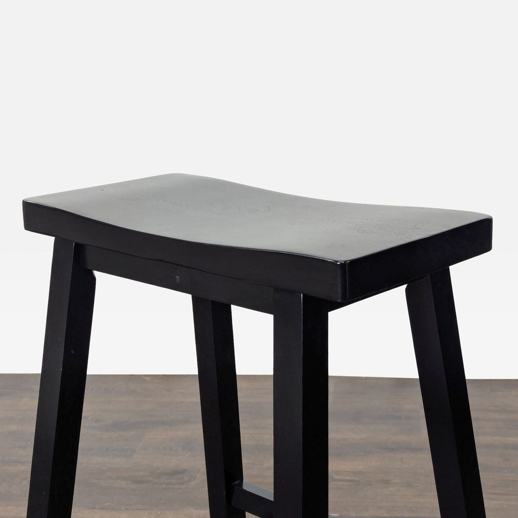 3. Close-up angle of a black wooden stool highlighting the curved seat and sturdy legs on a wood floor.