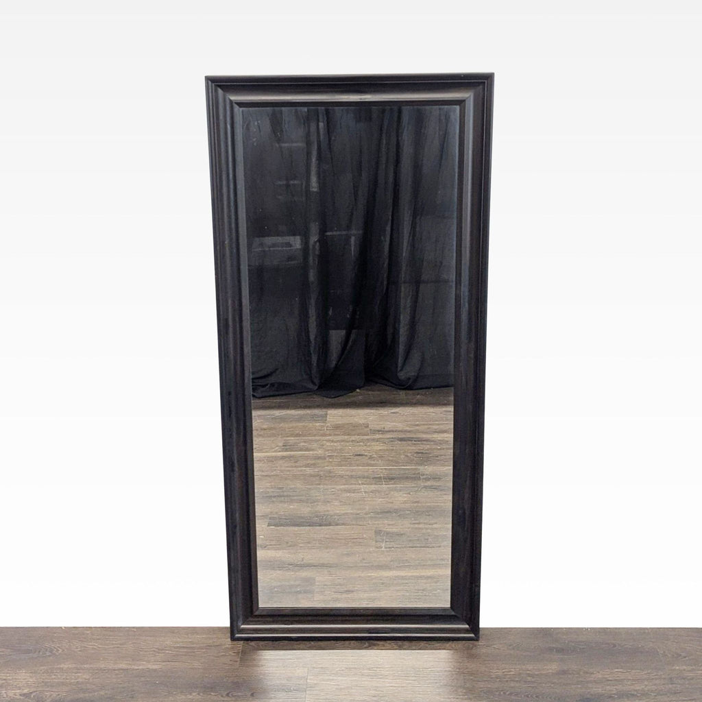 1. Full-length Ikea mirror with a dark wood frame standing on a wooden floor, reflecting black curtains.