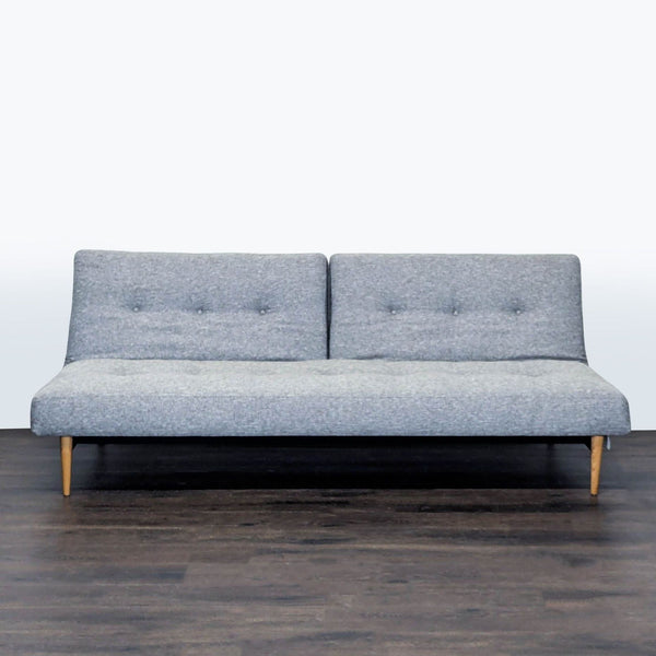 West Elm gray sleeper sofa with a modern design, tufted cushions, and wooden legs, ideal for small spaces.