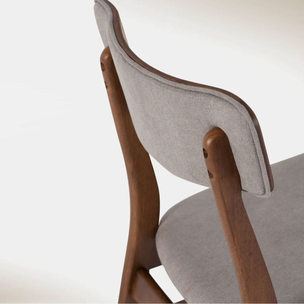 Close-up of the Hoft Home dining chair’s cushioned backrest and walnut-finished legs, highlighting fabric texture.
