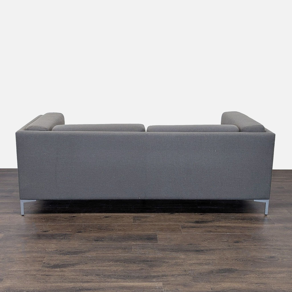 Boxy CB2 loveseat in deep gray fabric with sturdy metal legs; contemporary seating for small rooms or offices.