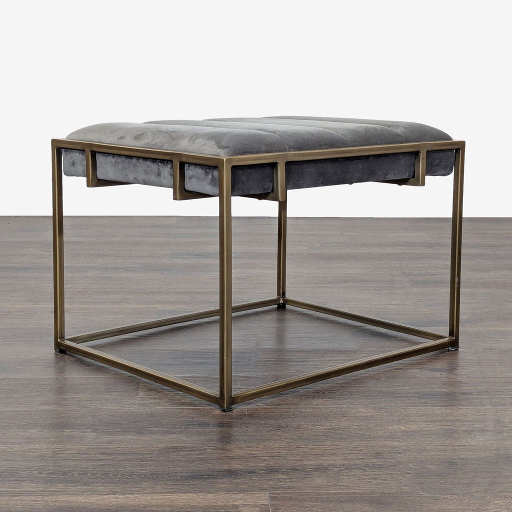 2. Square ottoman with a grey upholstered cushion and gold metal frame, angled side view on wood floor.