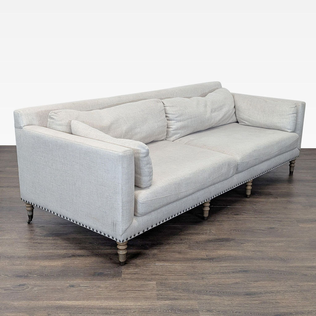 Neutral Pottery Barn sofa seats three, with large cushions, wooden legs, and stylish nailhead details.