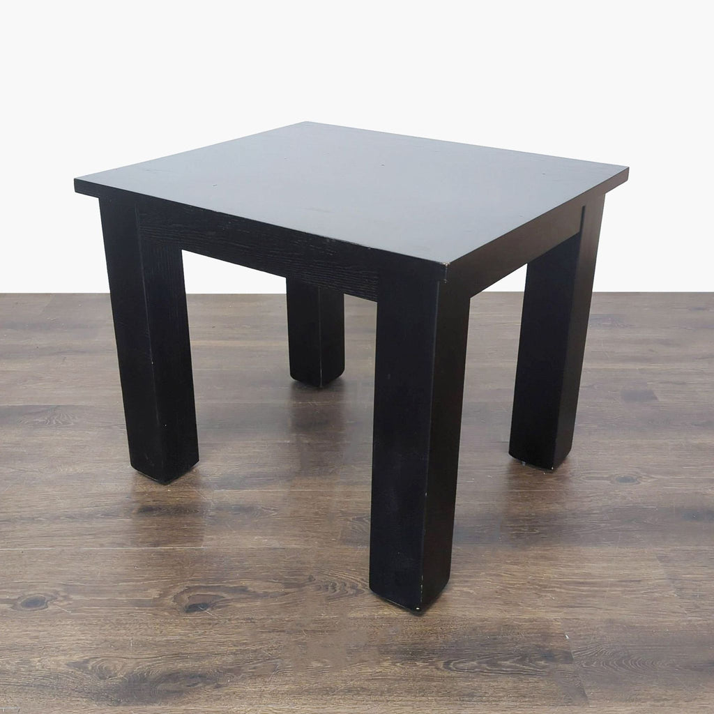 2. Perspective angle of a black end table with a smooth top and sturdy legs on a wooden floor.