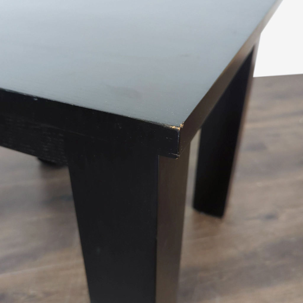 3. Close-up view of the corner of a black end table, highlighting its sleek lines and minor wear.