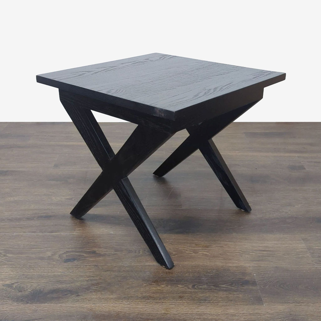 1. Black wooden end table with a square top and crossed X-shaped legs, shown on a wood floor.