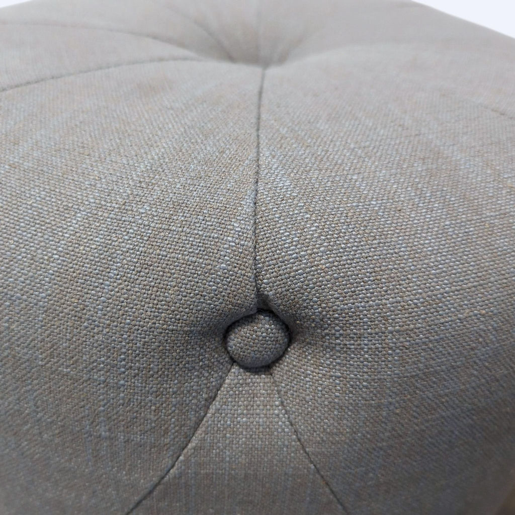 Close-up of a textured, tufted fabric surface with a centered fabric-covered button, part of a West Elm ottoman.  