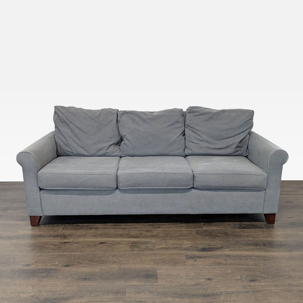1. Front view of a Pottery Barn 3-seat sofa with soft gray fabric, rolled arms, and wooden legs.
