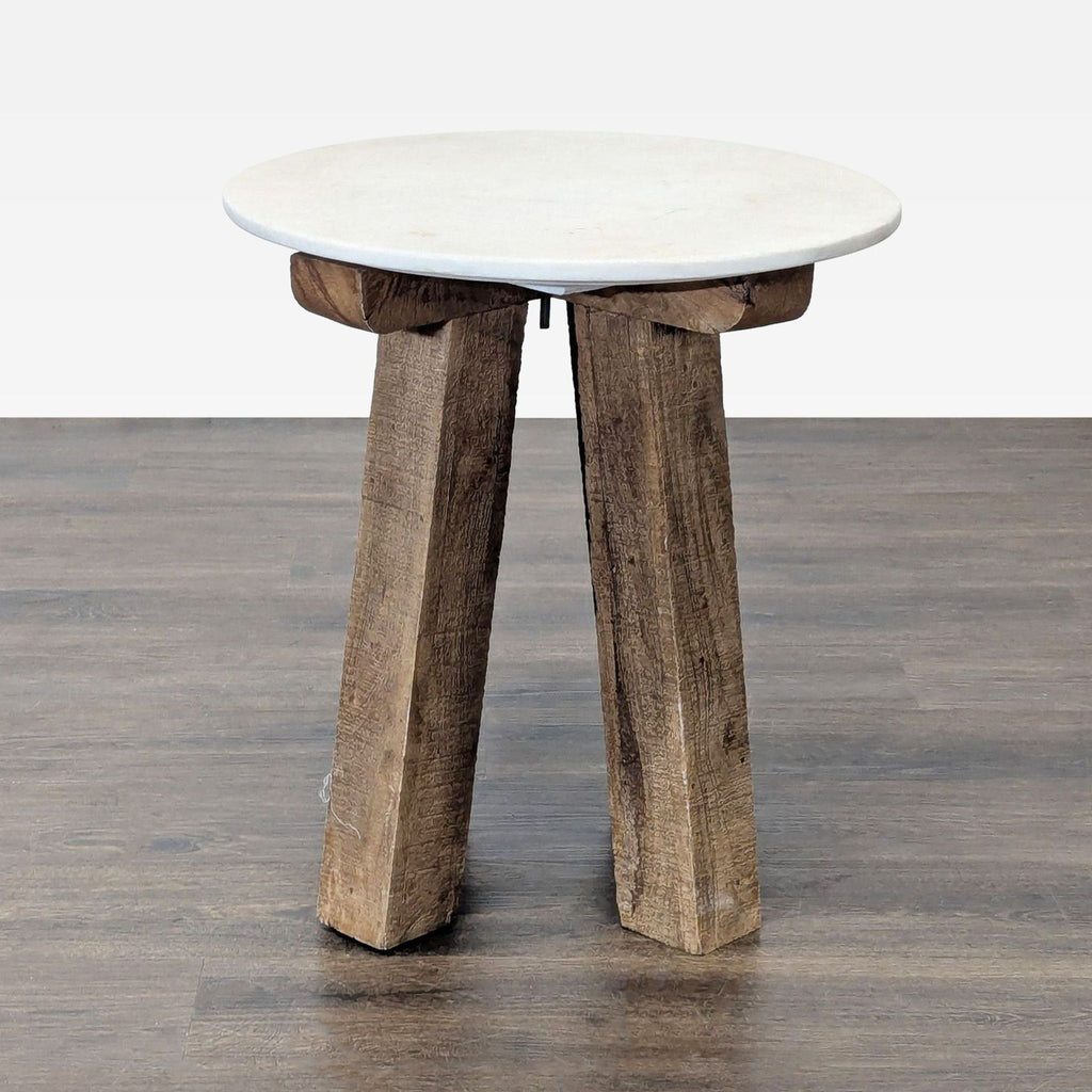 1. Round Anthropologie side table with a white top and chunky wooden legs on a dark wooden floor.
