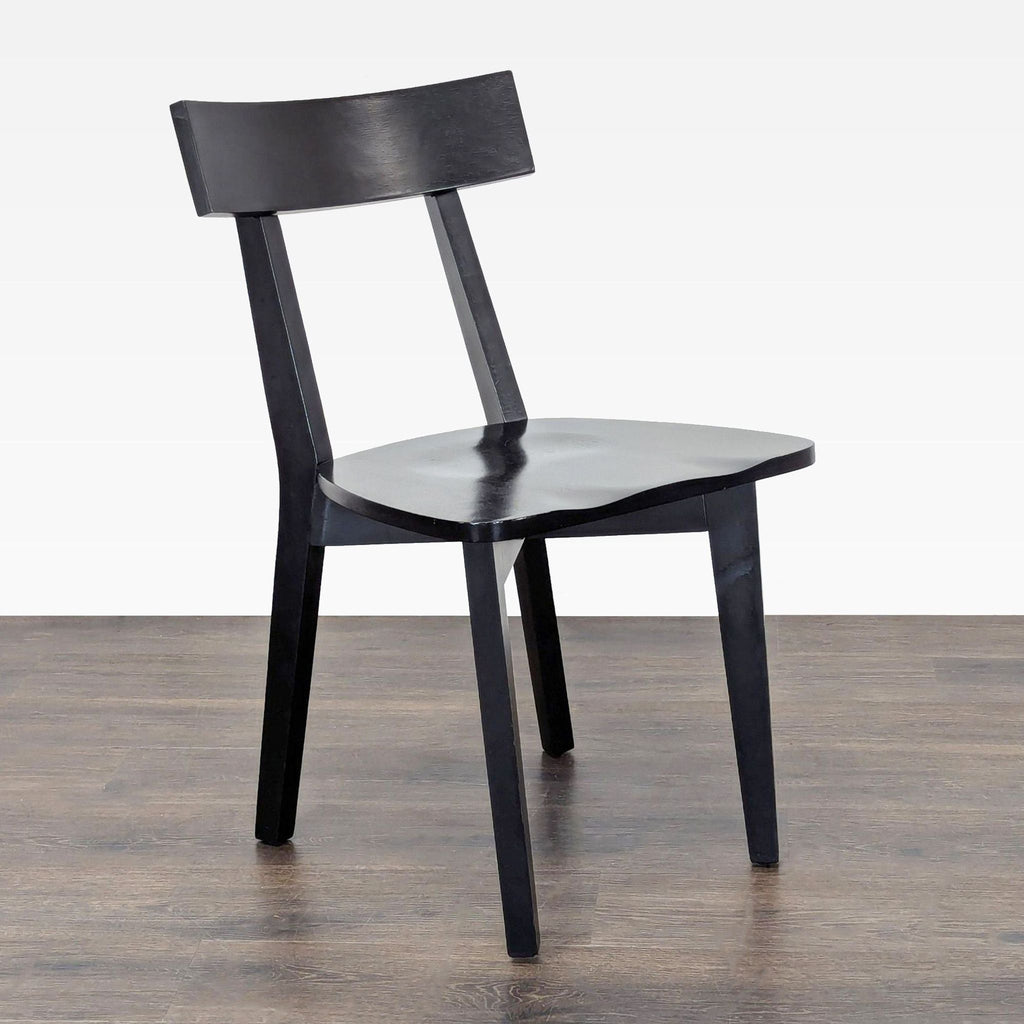 3. Angled view of a black wooden dining chair showing its minimalist design and gently scooped seat.