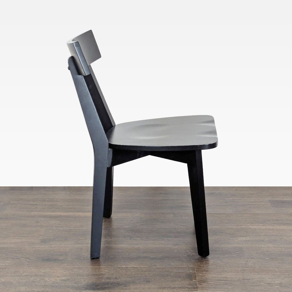 2. Side profile of a black wooden dining chair, highlighting the contoured seat and angled backrest.