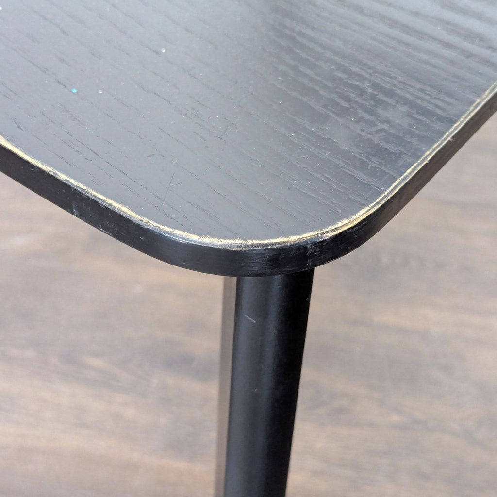Close-up of a black wood IKEA dining chair seat showing rounded corner and subtle wood grain texture.  