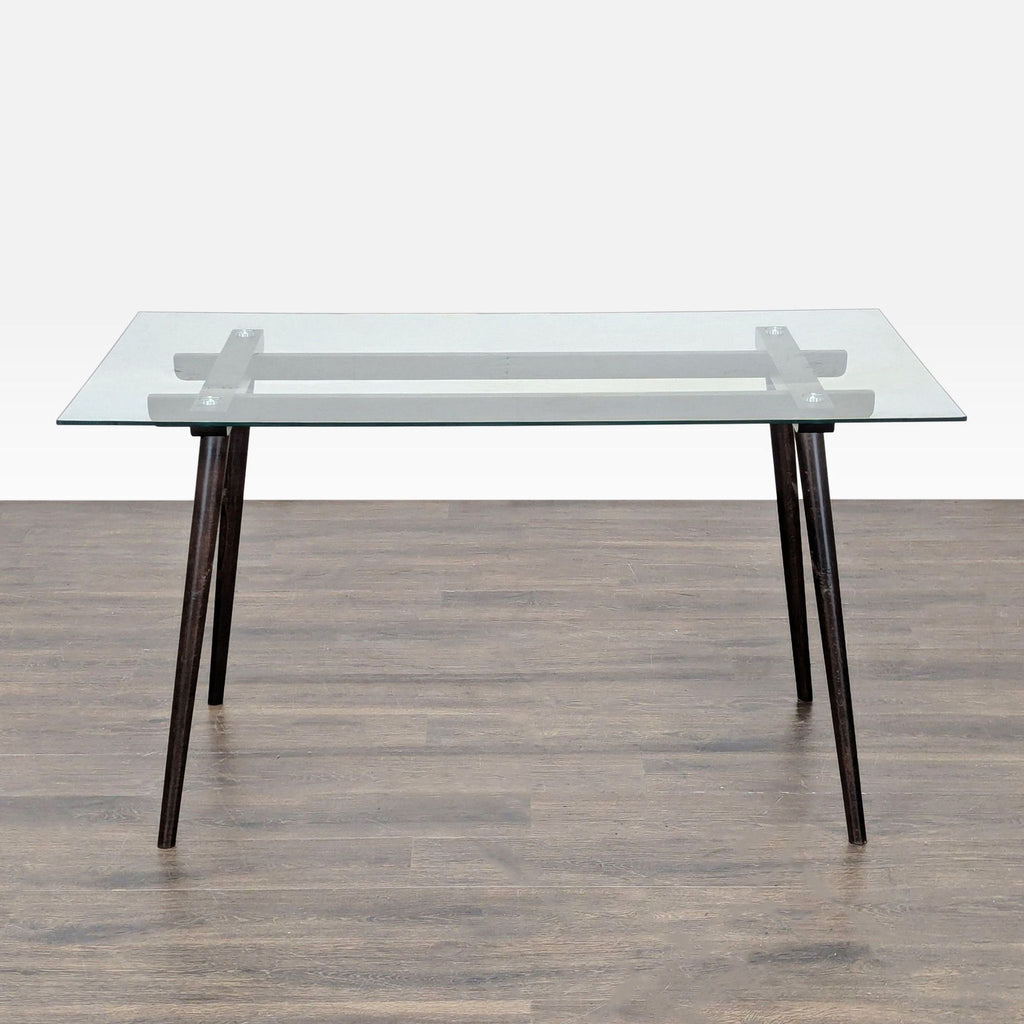 1. Rectangular dining table with a clear glass top and angled dark wooden legs, shown on a wood floor.