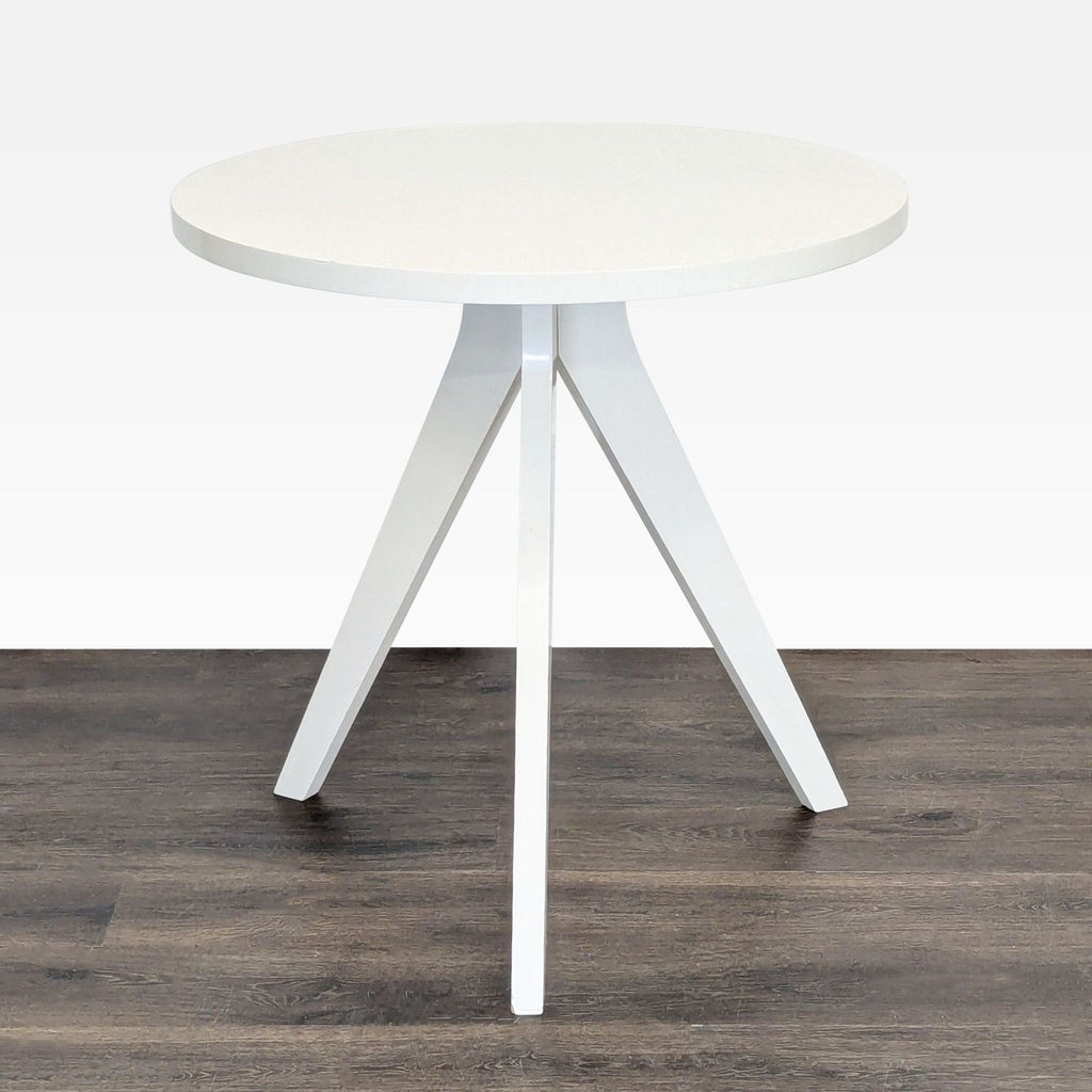1. Round white West Elm dining table with three angled legs, placed on a dark wood floor.