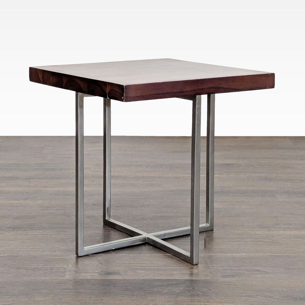 1. Modern end table with a thick square wood top and sleek metal cross legs, shown on a wood floor.  