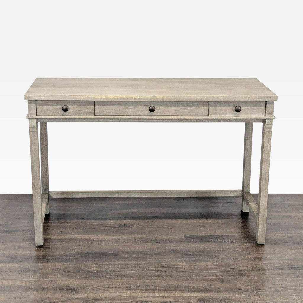 Light gray wooden desk with three drawers and metal knobs, ideal for a modern home office.