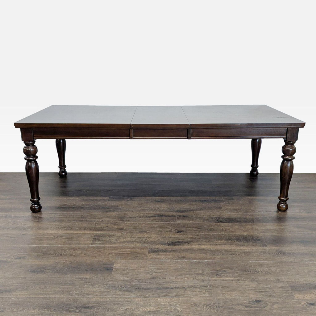 Rectangular Ashley Furniture dining table with turned legs and rich dark wood finish, no chairs shown.  