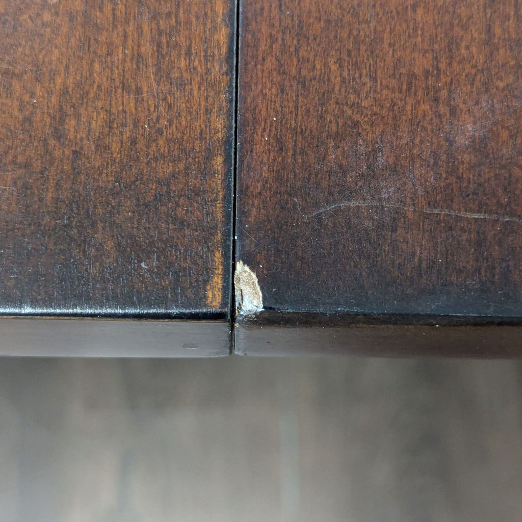 Close-up of a chip on the edge of a dark wood Ashley Furniture dining table from a dining set.