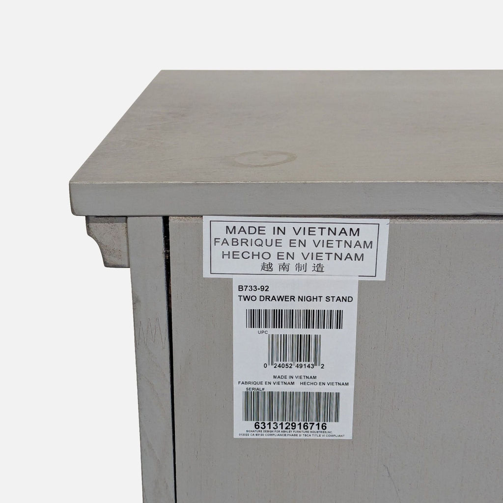 Modern end table in light gray with inlaid panels, two drawers, bun feet, and a concealed pull-out tray.