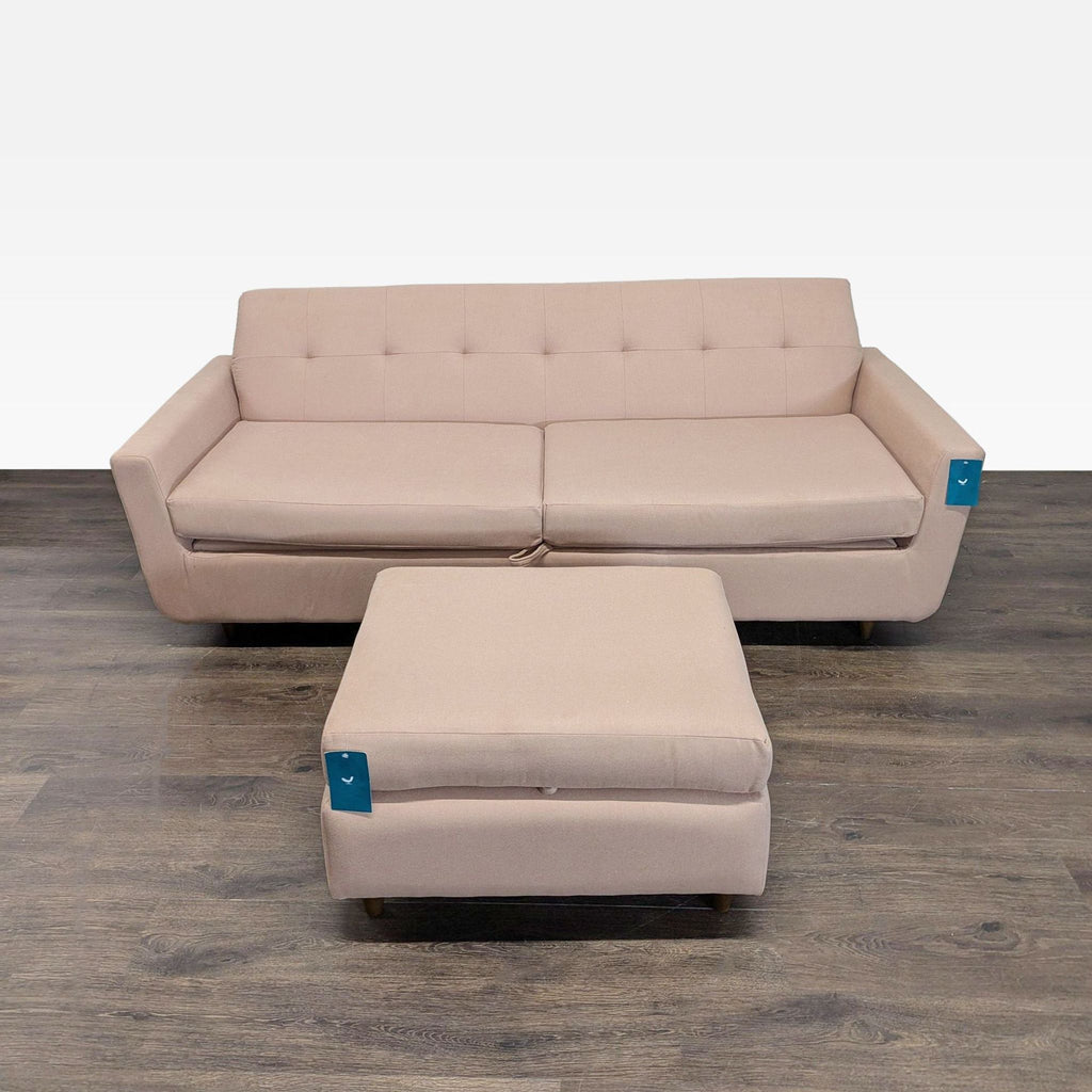 1. Beige 3-seat Joybird sofa with matching ottoman on dark wood floor, straight-on view.