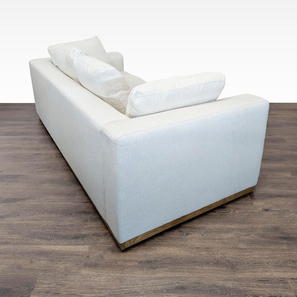 Rear perspective of a West Elm 3-seat sofa in cream, displaying its minimalist lines and sturdy wooden base.
