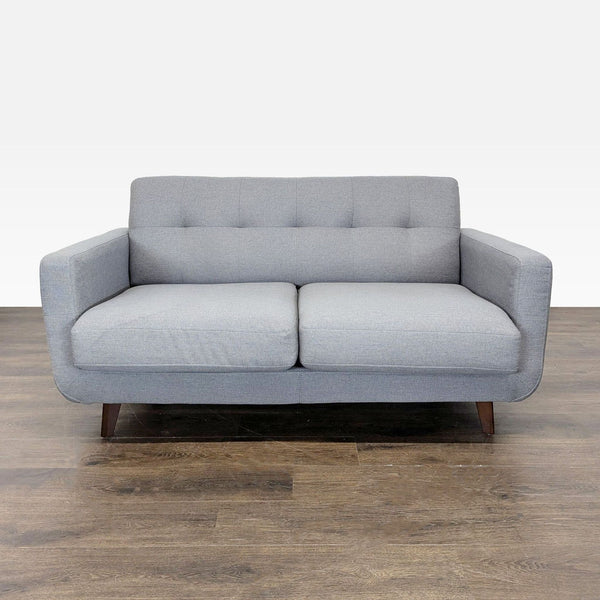 Light gray Living Spaces loveseat with cushioned seats, wooden legs, and a modern, clean-line design.