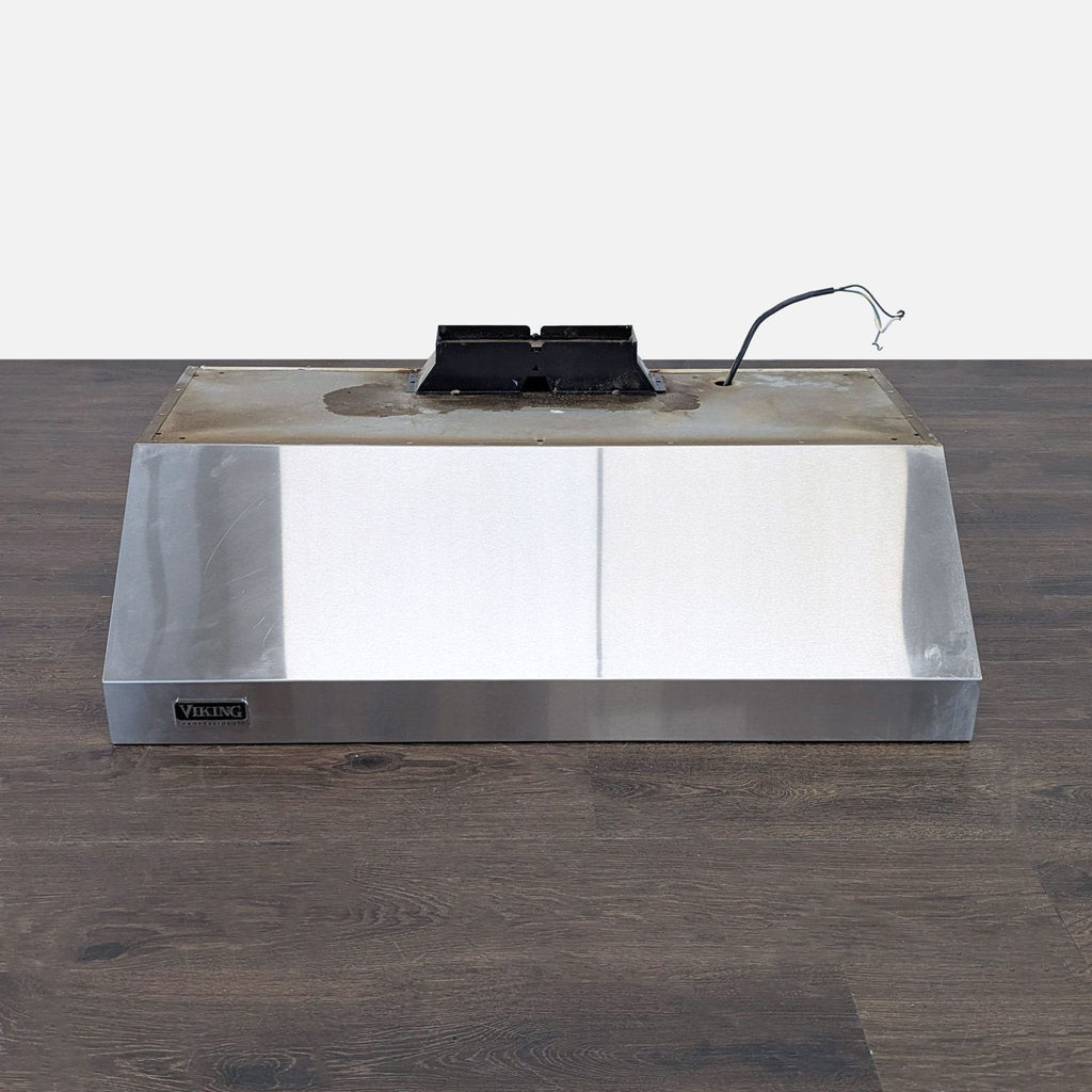 1. Stainless steel Viking range hood placed on a wood floor, showing a worn top and exposed wiring.