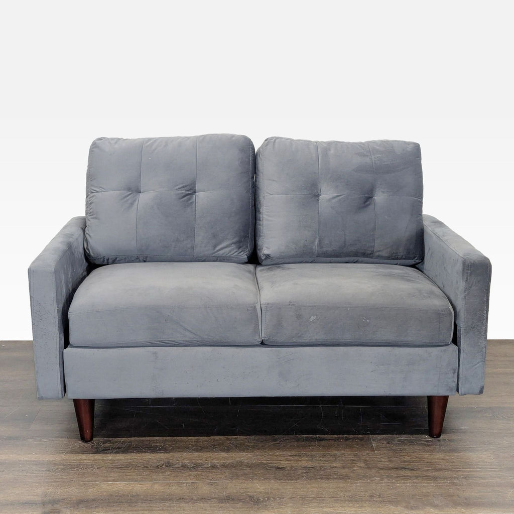 Gray velvet loveseat with tufted cushions and wooden legs, offering modern style and cozy comfort.